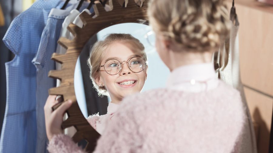 blondes mädchen mit brille schaut in den spiegel