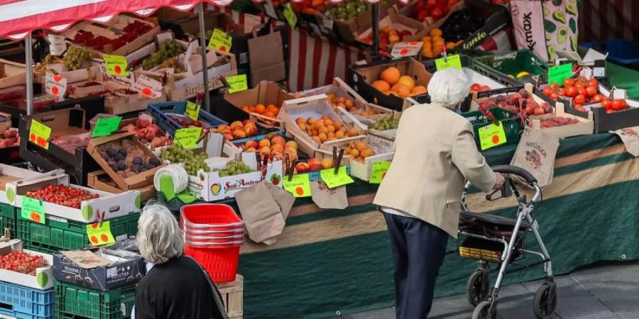 Eine Seniorin steht, gestützt auf ihren Rollator, vor einem Obst- und Gemüsestand auf einem Wochenmarkt. Foto: Jan Woitas/dpa-Zentralbild/dpa