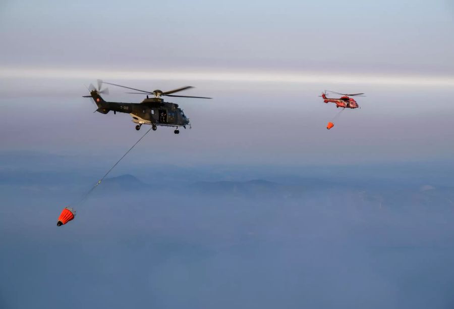 Mit den gefüllten Behältern leitet der rote griechische Helikopter die Schweizer Super Pumas zu den Brandherden.