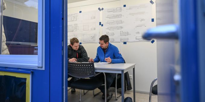 Dietrich und Altwegg bereiten sich auf die bevorstehende Bausitzung vor. Zwei Männer in einer Baubaracke
