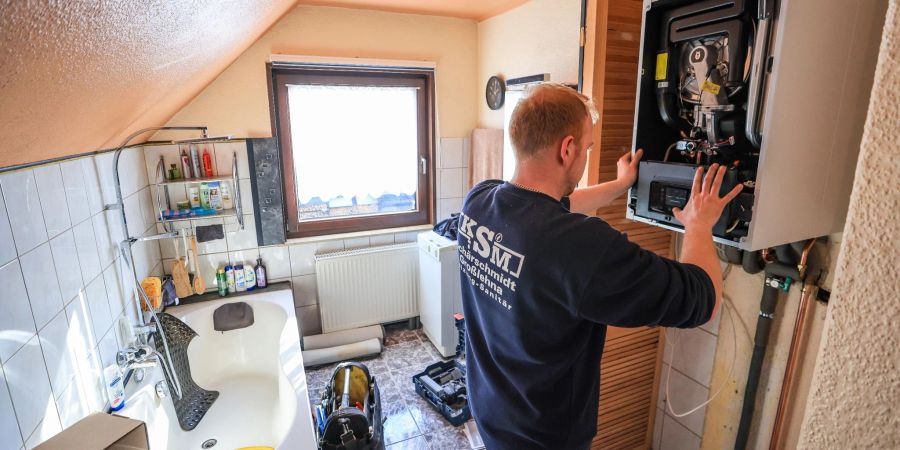 Ein Mitarbeiter einer Sanitär- und Heizungsbaufirma installiert eine moderne Gasbrennwerttherme in einem Einfamilienhaus.