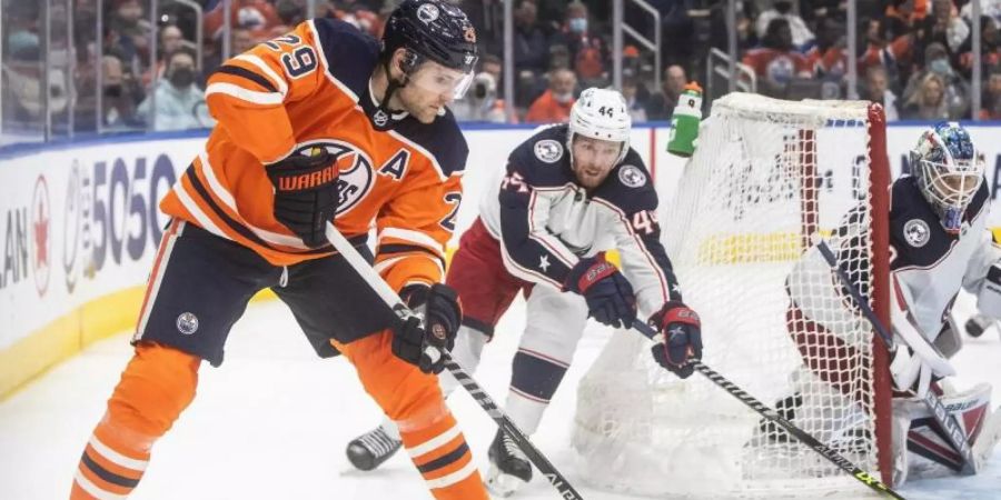 Vladislav Gavrikov (M) von den Columbus Blue Jackets in Aktion mit Leon Draisaitl (l) von den Edmonton Oilers und Torwart Elvis Merzlikins (r). Foto: Jason Franson/The Canadian Press via ZUMA/dpa