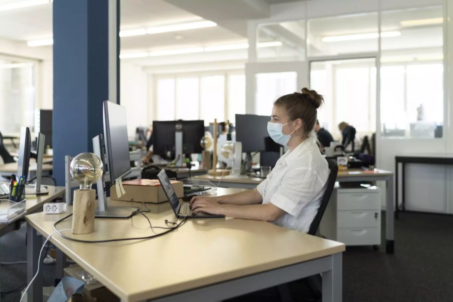 Eine Frau arbeitet im Büro mit einer Schutzmaske. (Symbolbild)