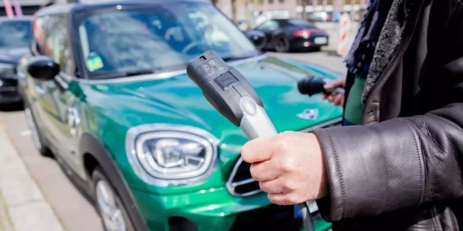 Ein Mann entfernt an einem Auto mit Plug-in-Hybrid-Antrieb in Berlin-Mitte das Ladekabel (Symbol). Foto: Christoph Soeder/dpa