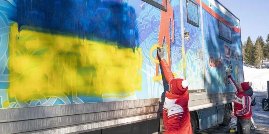 Mitglieder der russischen Langlauf-Nationalmannschaft versuchen, eine ukrainische Flagge und den Schriftzug «Ruhm für die Ukraine» zu entfernen. Foto: Torstein Boee/NTB Norway/AP/dpa