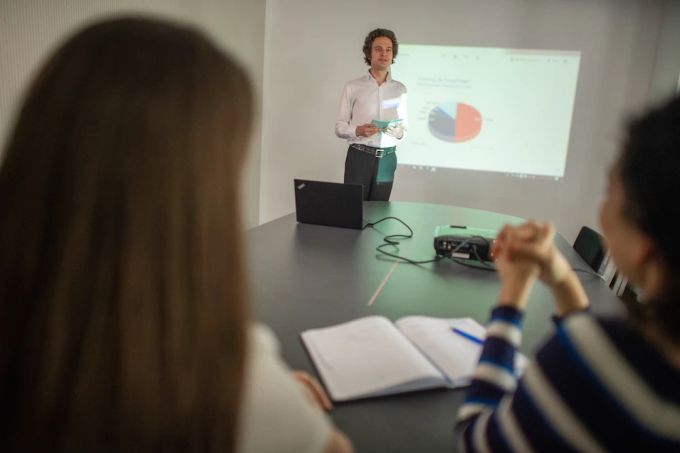 Kein guter Vortrag ohne guten Vortragenden: Wer überzeugen will, sollte sich auf wenige Kernbotschaften konzentrieren. Mann präsentiert vor Leinwand.