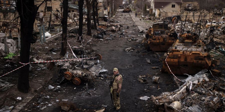 Ein ukrainischer Soldat steht in Butscha neben zerstörten russischen Panzern. Nach dem Rückzug der russischen Truppen kamen dort zahlreiche Kriegsverbrechen ans Licht.