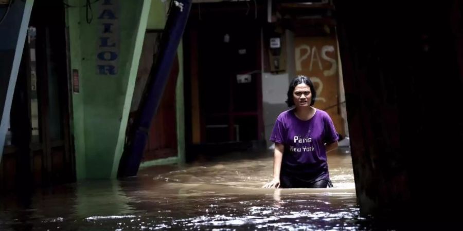 Eine Frau watet durch das Hochwasser einer überschwemmten Strasse in Jakarta. Foto: Tatan Syuflana/AP/dpa