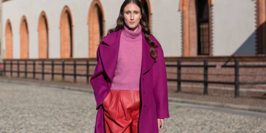 Streetstyle Frau in pinkem Mantel, rosa Top und Lederhosen.