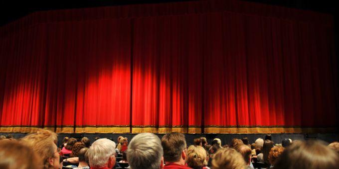 Eine Theatervorstellung ist unterhaltsam – auch alleine. Roter Theatervorhang, Bühne und Zuschauer.