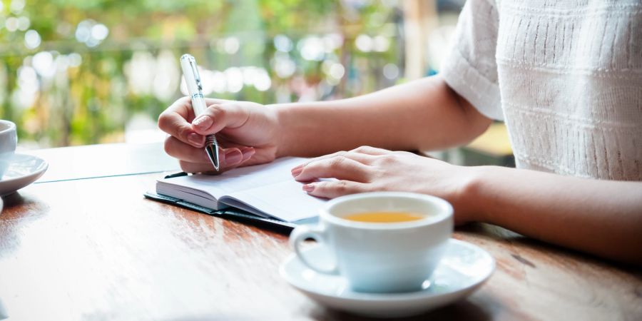 frau schreibt in ein notizbuch, tisch