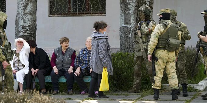 Ältere Anwohner sitzen im Ukraine-Krieg neben einer Gruppe russischer Soldaten in Cherson. Dieses Foto wurde während einer vom russischen Verteidigungsministerium organisierten Reise aufgenommen. Cherson