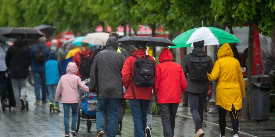 Spaziergänger sind mit Regenschirmen auf der Strandpromenade im Ostseebad Binz unterwegs. Graue Wolken, Regen und Wind sorgen für kühles Wetter an der Küste.