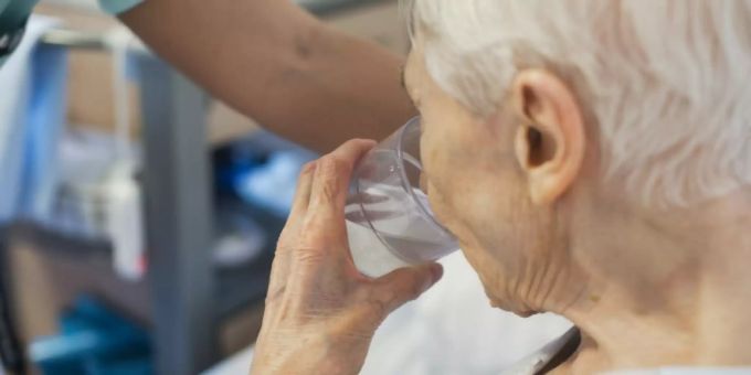 Eine alte Frau trinkt ein Glas Wasser. SPO