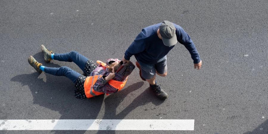 Ein Verkehrsteilnehmer (r) zieht bei einer Blockade der Letzten Generation auf der Autobahn 100 eine Aktivistin von der Strasse. Erneut hat die Klimaaktivistengruppe an zahlreichen Stellen in der Stadt Strassen blockiert.