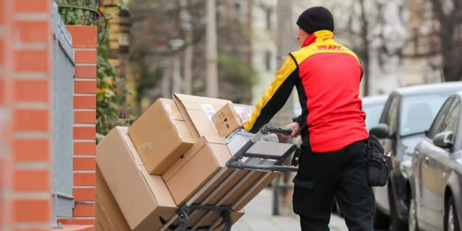 Ein DHL-Paketzusteller geht mit einer Sackkarre voller Pakete zu einem Haus. Foto: Jan Woitas/zb/dpa