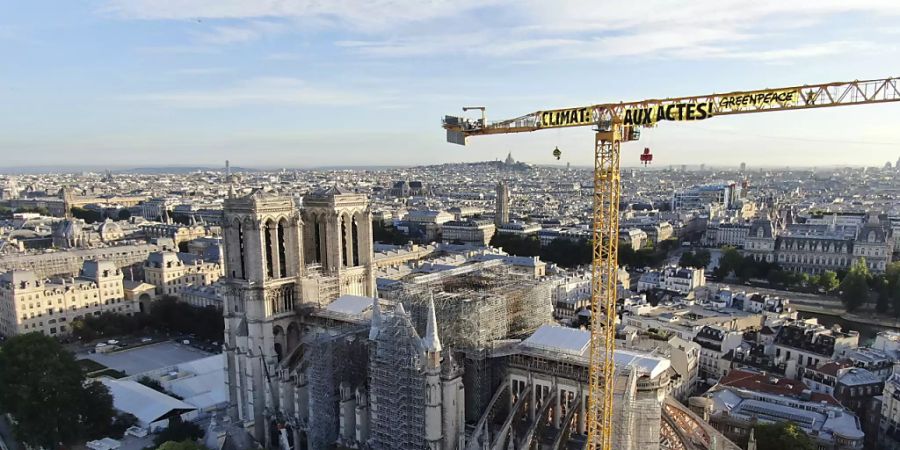 HANDOUT - Ein Transparent: «Klima. In Aktion» ist an einem Kran an der Baustelle der Kathedrale Notre Dame befestigt. Mit einer Aktion auf der Baustelle der Kathedrale Notre-Dame hat die Umweltschutzorganisation Greenpeace in Paris für Aufsehen gesorgt. Foto: Uncredited/Greenpeace/AP/dpa - ACHTUNG: Nur zur redaktionellen Verwendung und nur mit vollständiger Nennung des vorstehenden Credits