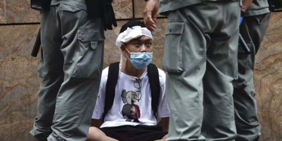 Bereitschaftspolizisten stehen im Hongkonger Central District um einen auf dem Boden sitzenden Demonstranten. Foto: Kin Cheung/AP/dpa