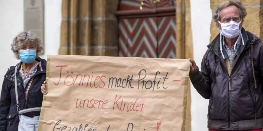 Demonstranten halten während einer Mahnwache zur Situation beim Fleischwerk Tönnies auf dem Marktplatz in Rheda-Wiedenbrück ein Schild mit der Aufschrift «Tönnies macht Profit - unsere Kinder bezahlen den Preis!». Foto: David Inderlied/dpa