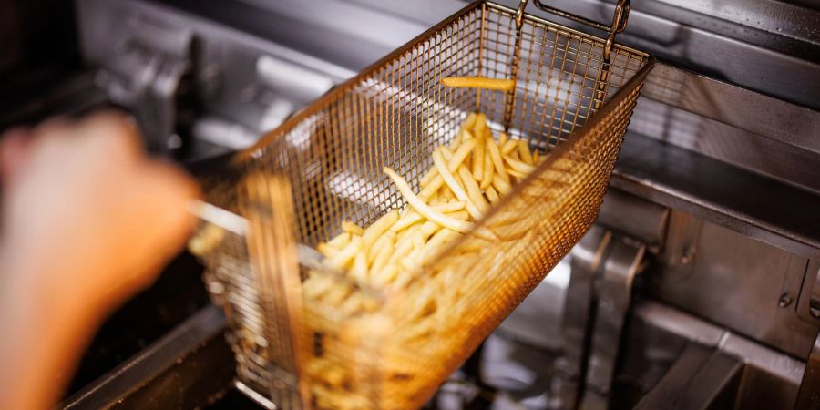 Eine Mitarbeiterin einer Münchener Filiale der Fastfoodkette McDonald's nimmt in einen Korb mit Pommes Frites aus der Friteuse.