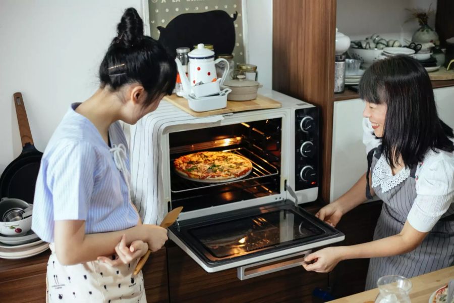 Frauen backen eine Pizza.