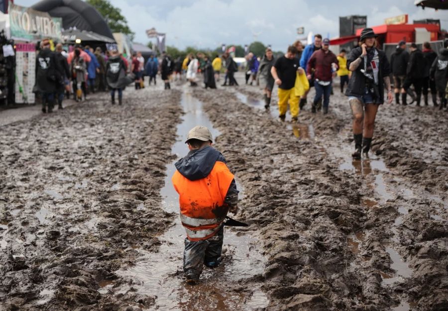 Mit Gummi-Stiefeln und Regenhosen bewaffnet, bahnen sich Metal-Fans ihren Weg durch das schlammige Festivalgelände.