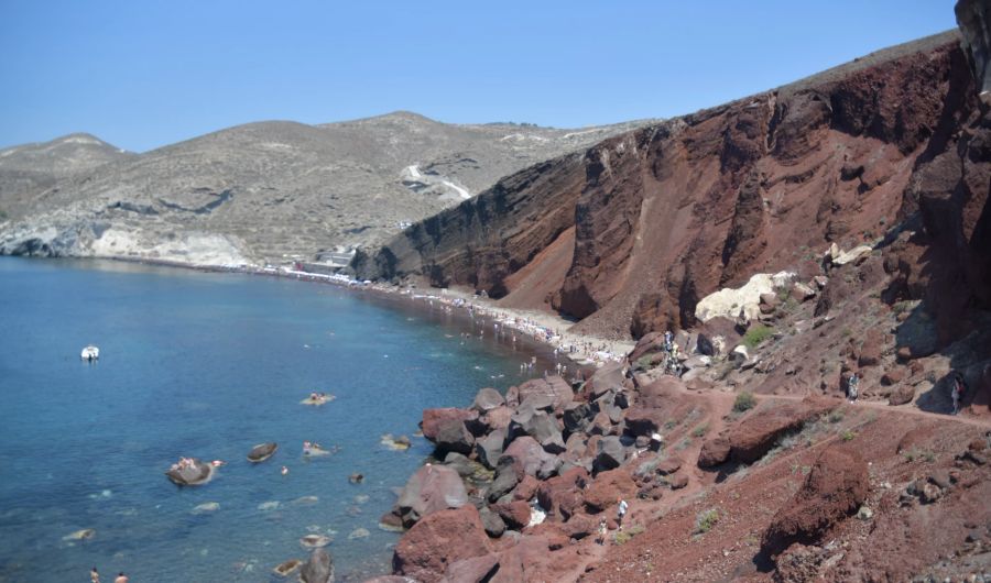 Im Hintergrund der etwa 200 Meter lange Lavakiesstrand vor der rot schimmernden Felswand. Rechts der Zugangsweg.