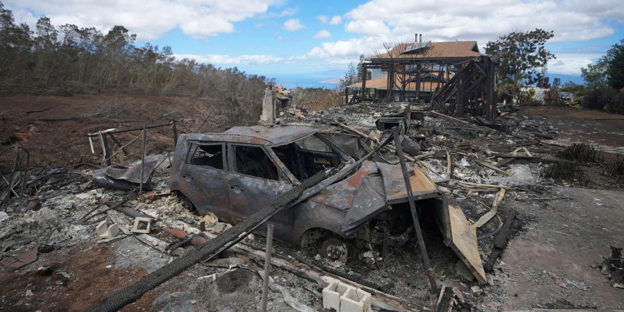 Die verkohlten Überreste eines Fahrzeugs stehen  in Kula neben einem von einem Waldbrand zerstörten Haus.