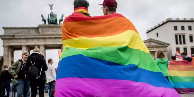 Eingehüllt in eine Regenbogenflagge, steht ein homosexuelles Paar vor dem Brandenburger Tor in Berlin. Gen