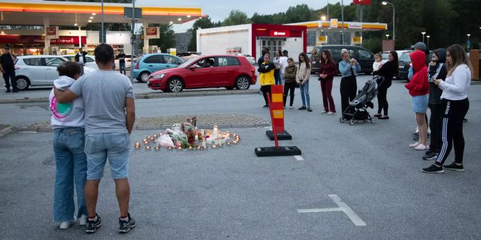 Menschen stehen neben Blumen und Kerzen auf einem Parkplatz nahe einer Tankstelle in Stockholm. Stockholm
