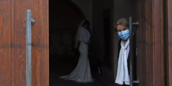 Eine Frau, die eine Mund-Nasen-Bedeckung trägt, hält eine Tür für eine Hochzeit in Prag geöffnet. Tschechien Prag