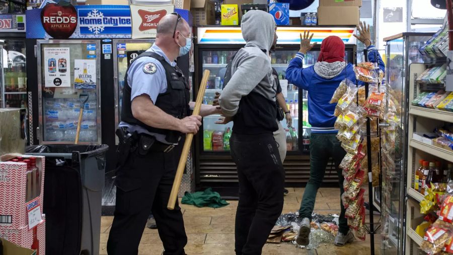 EinBei den Protesten kam es auch zu mehreren Plünderungen. Polizeibeamter verhaftet zwei Männer, die sich im Lagerraum eines Spirituosengeschäfts versteckt hielten.