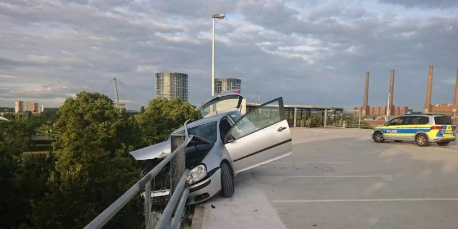 Das Auto hängt in der Sicherungsplanke auf einem Parkhausdeck in Wolfsburg. Foto: -/Polizei Wolfsburg/dpa