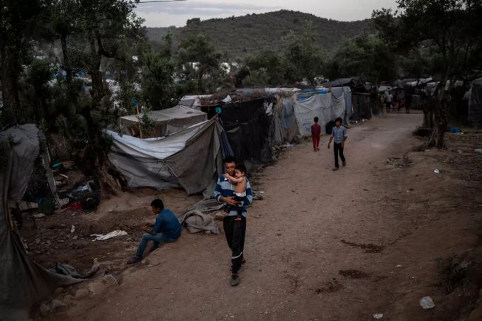 Ein Geflüchteter läuft mit einem Kind durch ein Übergangslager neben dem Flüchtlingslager Camp Moria. Geflüchtete auf Lesbos