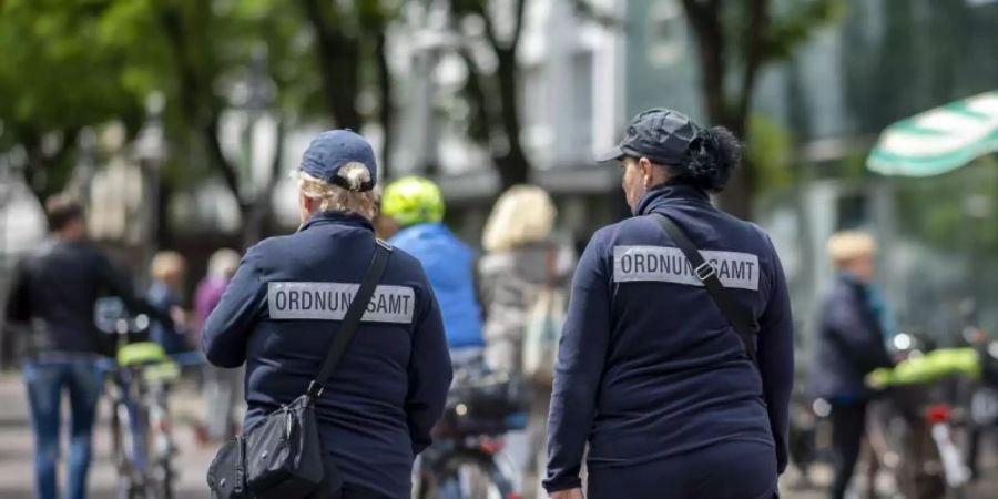 Zwei Mitarbeiterinnen vom Ordnungsamt kontrollieren in der Berliner Strasse in der Innenstadt von Güterloh. Foto: David Inderlied/dpa