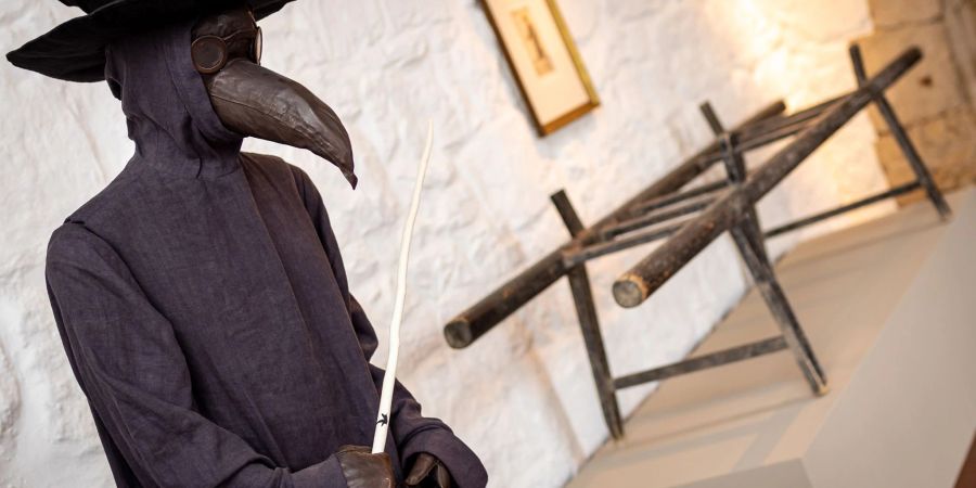 Die Figur eines Pestdoktors mit einer Schnabelmaske steht neben einer Pestbahre, die aus dem Jahr 1682 stammt.