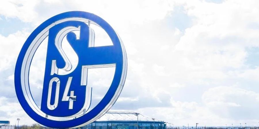 Im Vordergrund dreht sich das Logo des FC Schalke auf der Geschäftsstelle, im Hintergrund steht die Veltins-Arena. Foto: Guido Kirchner/dpa