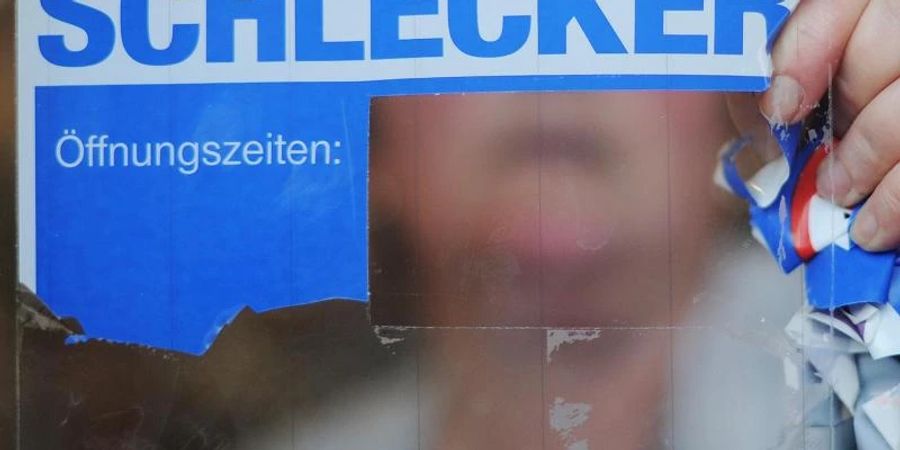 Eine Schlecker-Mitarbeiterin reisst das Firmenlogo von der Eingangstür einer Filiale. Foto: picture alliance / Julian Stratenschulte/dpa