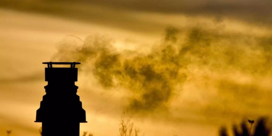 Ein kleiner Schornstein auf einem bepflanzten Dach entlässt bei Sonnenaufgang die Abgase einer Gasheizung in die eiskalte Morgenluft. Foto: picture alliance / dpa