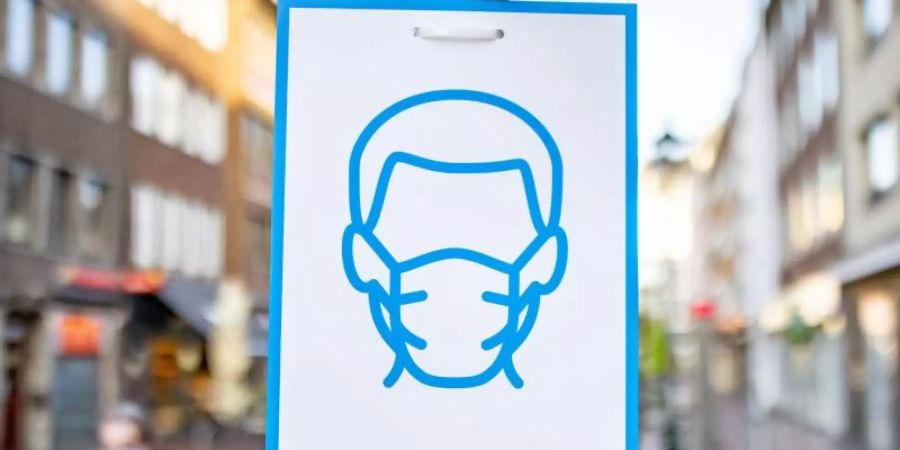 Ein Schild mit dem Symbol für Maskenpflicht an einem Strassenschild in der Innenstadt von Düsseldorf. Foto: Marcel Kusch/dpa