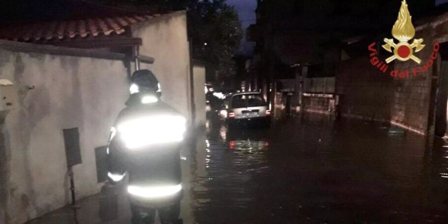 HANDOUT - Ein Feuerwehrmann steht in einer überfluteten Strasse auf Sardinien. Auf der italienischen Mittelmeerinsel hat ein Unwetter schwere Schäden angerichtet. Foto: Vigili del Fuoco/dpa - ACHTUNG: Nur zur redaktionellen Verwendung im Zusammenhang mit der aktuellen Berichterstattung und nur mit vollständiger Nennung des vorstehenden Credits