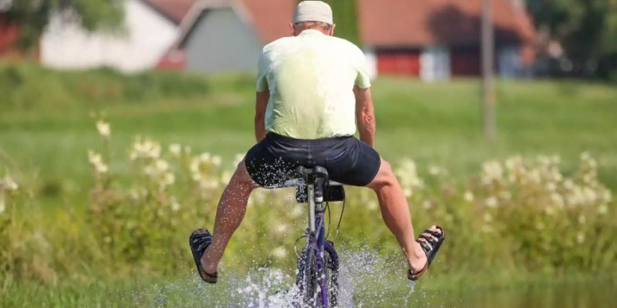 Ein Radfahrer fährt in Sandalen auf dem vom Regen überfluteten Donau-Radwanderweg durch das Hochwasser. Foto: Thomas Warnack/dpa