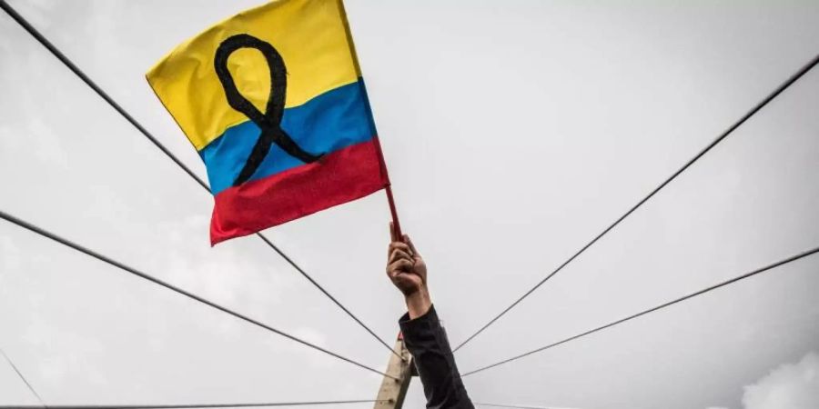 Ein maskierter Demonstrant schwenkt die kolumbianische Flagge. Foto: Juan Pablo Otalvaro M/dpa