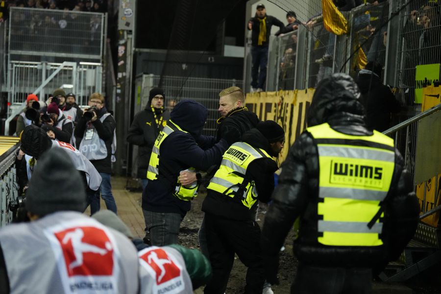 Ein Fan springt über den Zaun. Zunächst greifen die Ordnungskräfte ein.