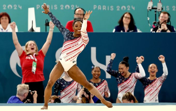 Simone Biles in der Boden-Übung bei Olympia 2024 – im Hintergrund feiert ihr Team schon den Triumph. Olympia 2024 Simone Biles