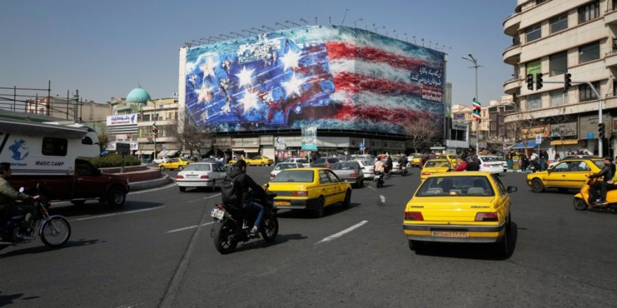 Fahrzeuge fahren an einer Werbetafel vorbei, auf der ein US-Flugzeugträger mit beschädigten Kampfjets an Deck abgebildet ist. Auf dem Enqelab-e-Eslami-Platz (Platz der Islamischen Rev...