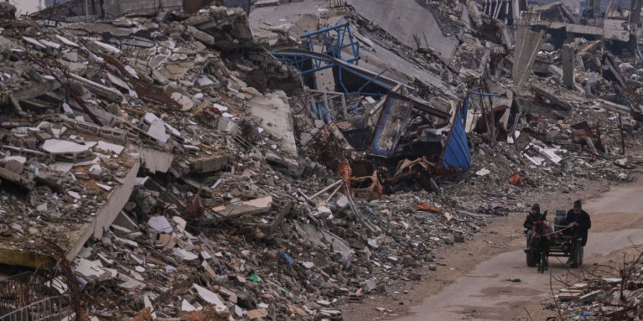 ARCHIV - Palästinenser gehen eine Straße in der Stadt Gaza entlang, die von Gebäuden umgeben ist, die bei israelischen Luft- und Bodenangriffen im Viertel Sheikh Radwan zerstört wur...