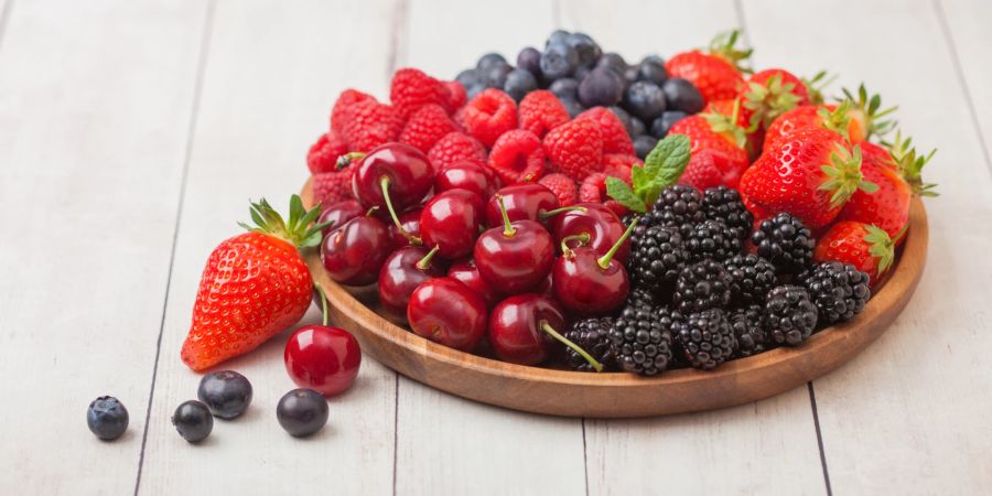 Sommerbeeren auf einem Holzteller auf weissem Holztisch.