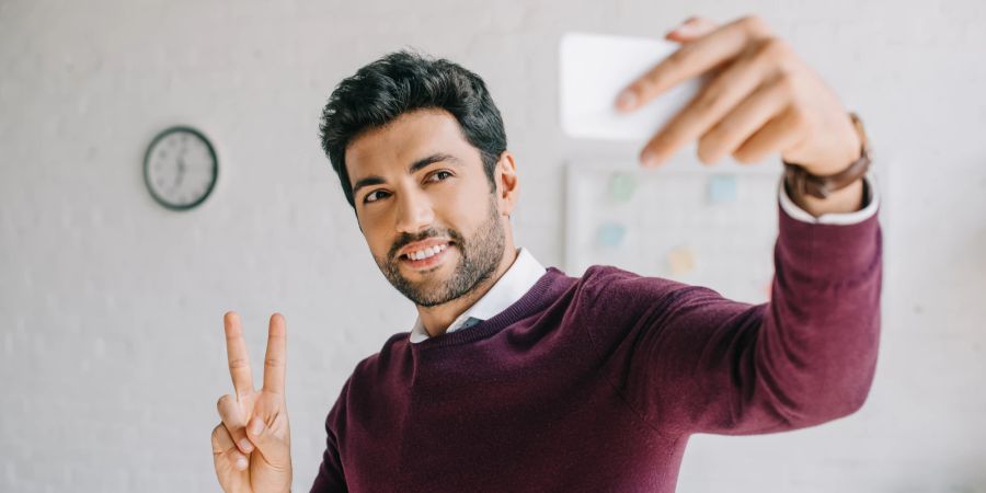 mann hält zwei finger in die höhe und fotografiert sich selbst