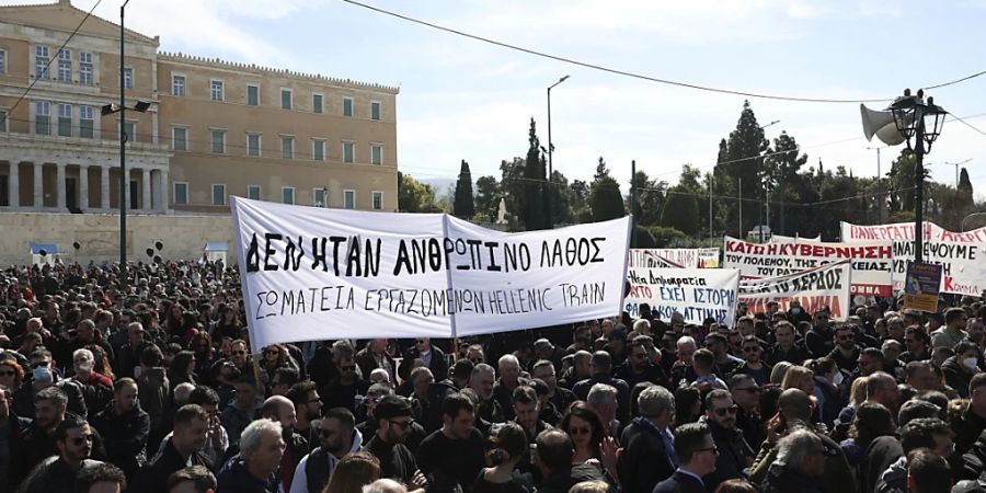 Menschen versammeln sich während einer Demonstration vor dem griechischen Parlament. Tausende Menschen protestieren seit dem schweren Zugunglück, der wegen falscher Weichenstellung in der Nacht zum Mittwoch (01.03.2023) mit einem Güterzug kollidierte. Auf dem Transparent steht «Es war kein menschliches Versagen». Foto: Yorgos Karahalis/AP